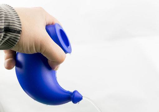 Use of a device for washing the nose. The hand holds the device with a pouring solution for rinsing on a white background.