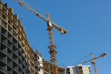 two yellow construction cranes running near the house under construction, the elements of the house frame