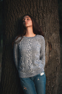 A young woman   with eyes closed is posing near tree.