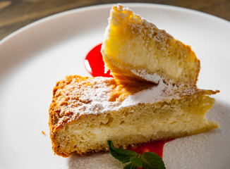 Piece of cake on plate with strawberry sauce on a wooden background