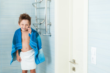 Fototapeta na wymiar funny cute small boy winks standing in the bathroom with a towel on his shoulders
