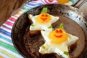 Fried eggs shaped as stars with funny faces in a pan