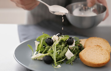 Woman dressing fresh vegetable salad with arugula leaves and olives