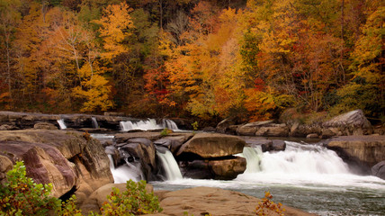 River waterfall over large rocks with Autumn scenery.