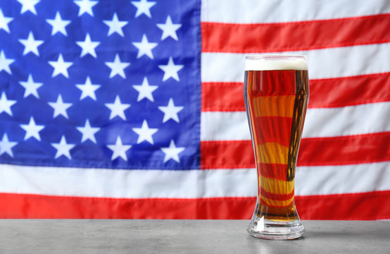 Glass of beer on table against blurred American flag