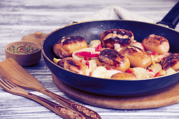 Fried pork sausages with apples and onions in a frying pan