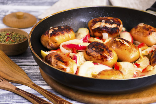 Fried pork sausages with apples and onions in a frying pan