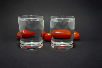 cherry tomatoes through two glasses with water on a black background