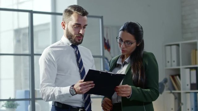 Young handsome businessman standing with female colleague in the office and discussing document on clipboard