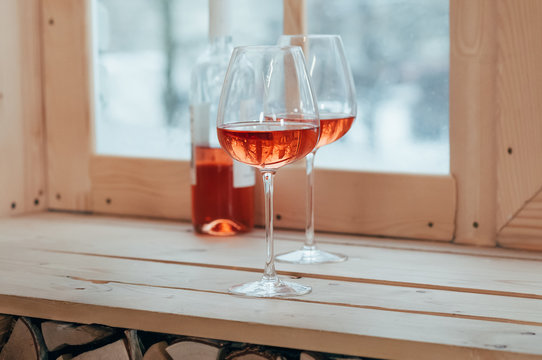 A bottle of rose wine and two filled glasses on a window sill