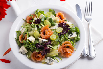 Delicious salad with salmon, grapes and cheese on a white background