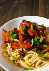 Boiled spaghetti with fried small pieces of meat on a wooden background