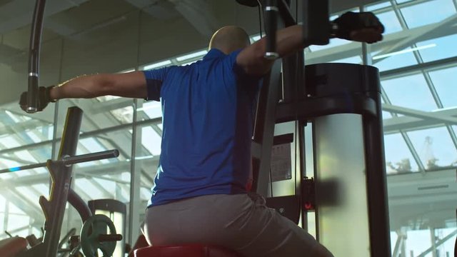 Mature man working out at the gym and doing reverse butterfly with exercise machine