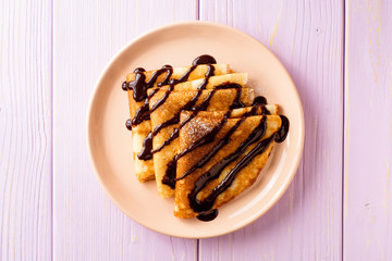 Crepes with chocolate syrup on purple wooden background.
