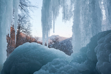 Fototapeta premium Bad Urach Wasserfall mit Eis und Blick auf die Burgruine Hohenurach. In der Eishöhle unter den Eiszapfen.