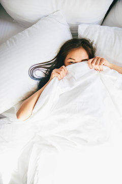 Young woman hiding under blanket in bed
