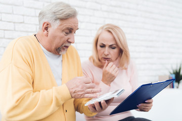 A couple of old people are sitting on the couch and are concentrating something.