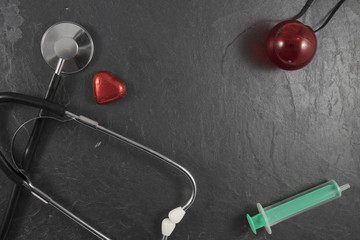 Stethoskop mit roter Nase, Herz und Spritze auf Schiefer