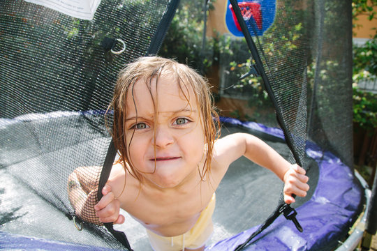 Little boy peering out of trampoline net screen with cute mad expression