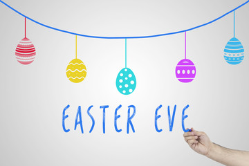 Human hand writing Easter eve against white board with drawn Easter eggs on a rope