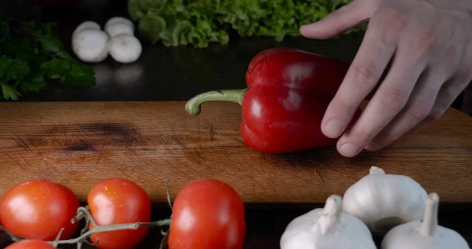 Kitchen table with vegetables, red pepper, tomato, green salad, champignons, garlic and knife.