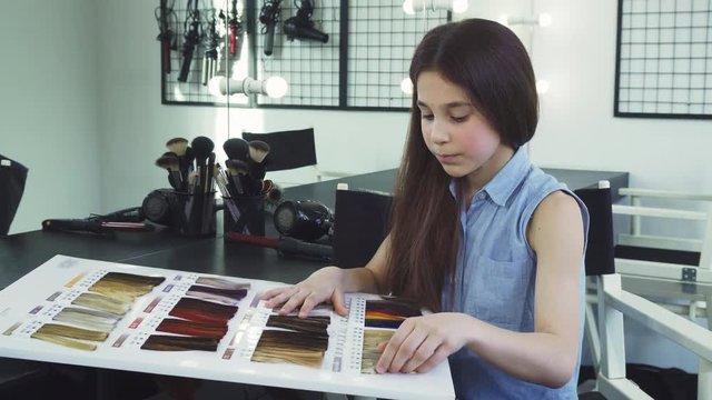 Beautiful little girl looking confused rubbing her chin choosing air color dye at the beauty salon fashion hairstyle hairdressing pampering lifestyle children kids leisure hairdo care.