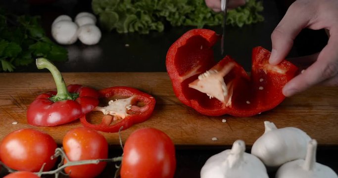 Kitchen table with vegetables, red pepper, tomato, green salad, champignons, garlic and knife.