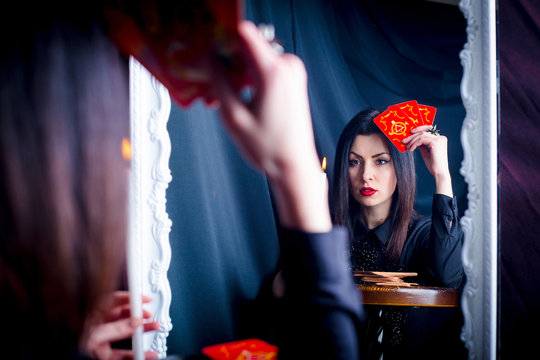 A woman with tarot cards and a candle looks into her reflection in the mirror. Prediction of the future, fortune telling.