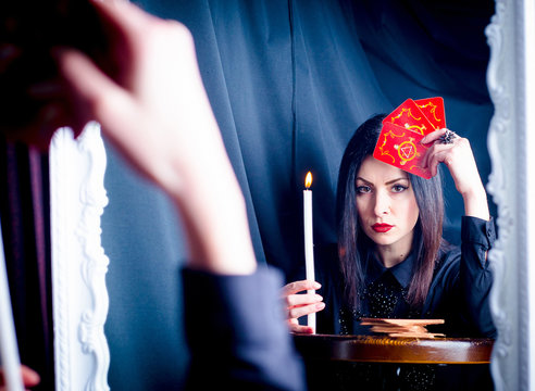 A woman with tarot cards and a candle looks into her reflection in the mirror. Prediction of the future, fortune telling.
