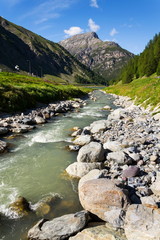 Spol River flowing in Lake Livigno with Corno Brusadella Mountain in background, Italy, sunny summer day