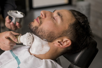Fototapeta premium Hairdresser shaving his beard with a razor to a client