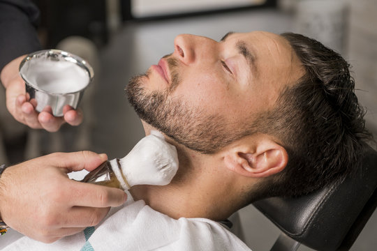 Hairdresser shaving his beard with a razor to a client