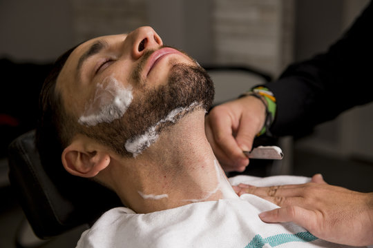 Hairdresser shaving his beard with a razor to a client