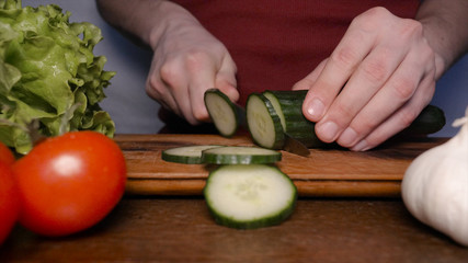 Kitchen table with vegetables, cucumber, tomato, green salad, garlic and knife.