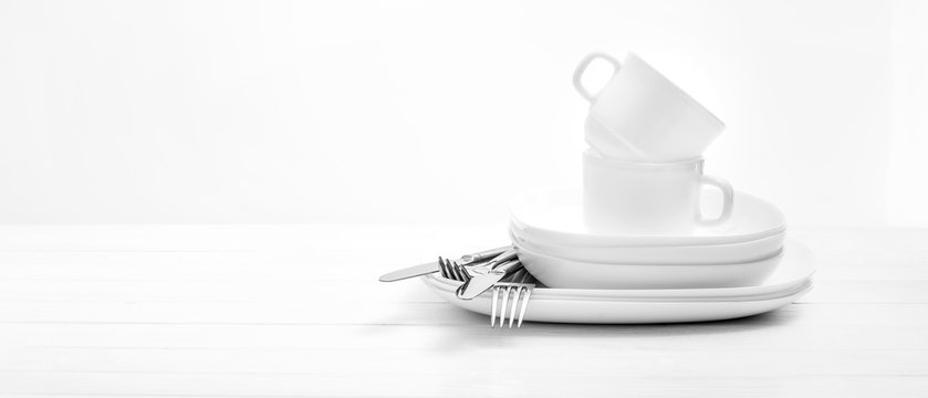 Plates, cups and silver cutlery on light white background