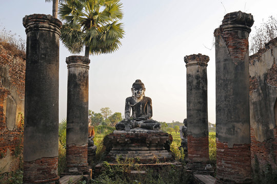 Old temple ruins and aged statue of a sitting Buddha viewed from the front at the Yadana Hsemee Pagoda complex in Inwa (Ava) near Mandalay in Myanmar (Burma) on a late afternoon.