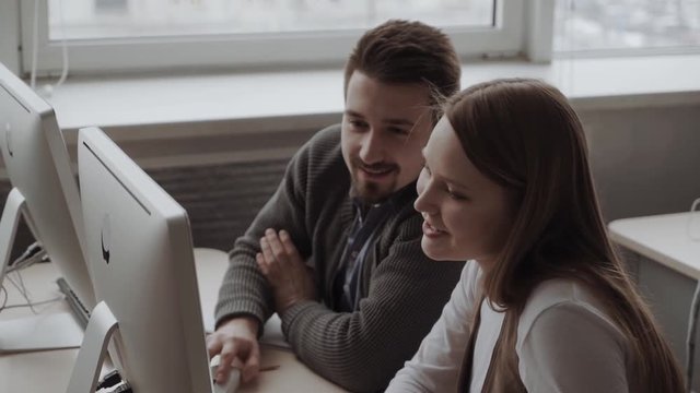 Young professional business team is working on a project, man is clarifying something. Smiling, looking at the computer screen