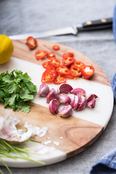 Garlic, red chillis and herbs being prepared on a cutting board.