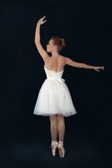 Naklejka premium the ballerina in pointes and a white dress dances on a dark background