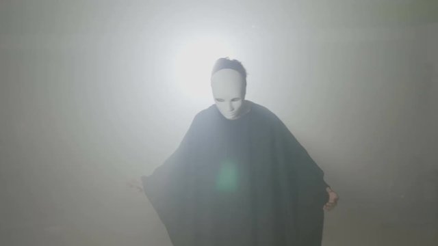 Actor presenting his evil simple halloween costume made from a dark cape and a white mask laughing maleficent