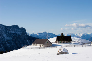 Snow covered alpine pasture with some cabins and a dramatic view over the mountains