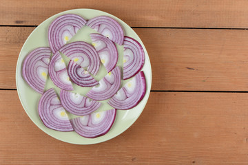 Violet bow on a green plate, onion on a dark wooden background, sliced onion laid out on a plate, vegetables in rustic style, minimalism, vegetarian product, vitamins, healthy food, art