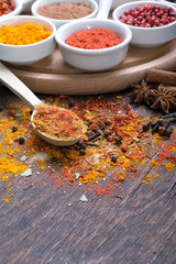 Colorful spices in spoons on dark wooden background