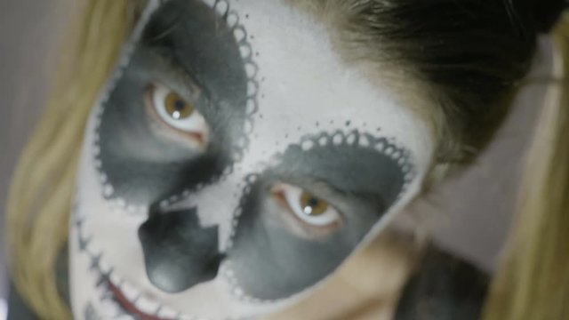 Close up face of young girl wearing halloween skull paint makeup and costume looking straight to camera