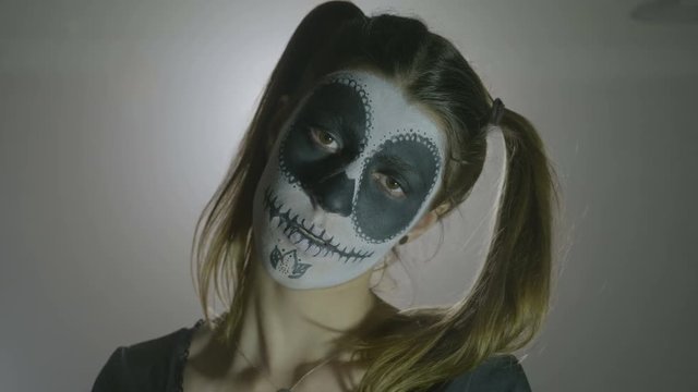 Portrait of a psycho halloween girl wearing doll costume shaking her skull head closing her eyes slowly and looking at camera