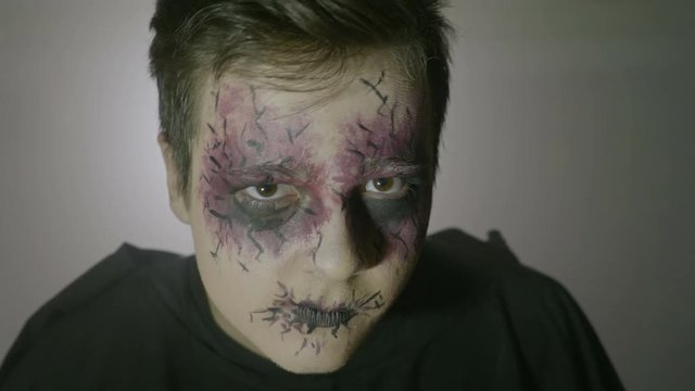 Portrait of a young psychopath zombie man with strange eyes and face paint doing frightening halloween moves