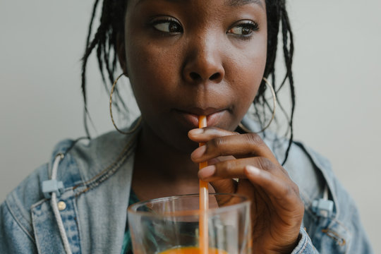 Young woman drinking cold pressed juice against simple backgroun