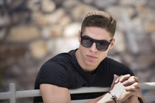 Man with sort ahir leaning lean on banister wear sunglasses looking away