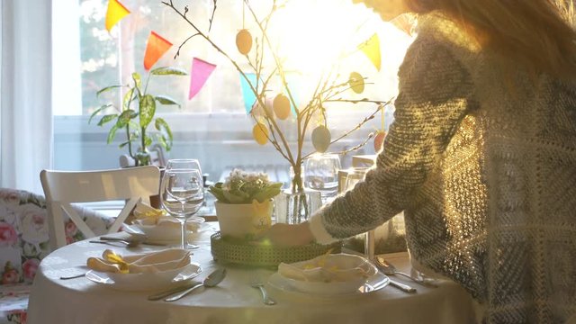 Young woman and her little daughter are setting easter festive table with bunny and eggs decoration