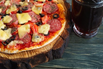 Delicious pizza with salami, mozzarella and olives and mug of dark beer, close up. Homemade culinary, snacks concept